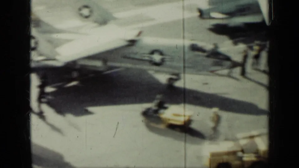 1962 Cuba frame of a carrier flight deck, showing jet aircraft, crew members, shadows, deck markings, and equipment in soft 8mm focus.