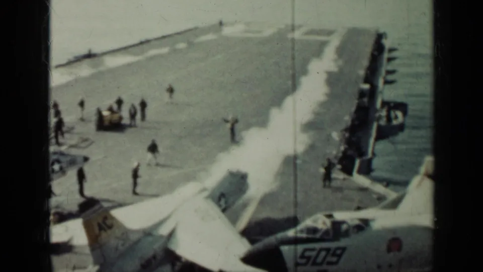 1962 Cuba-related home-movie frame showing U.S. Navy jets, deck crew, and flight deck activity on an aircraft carrier.