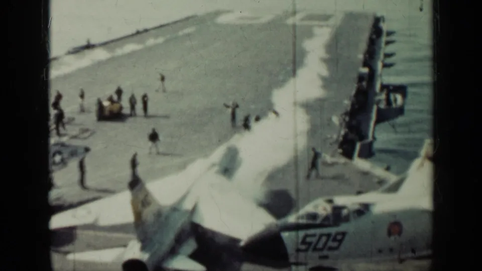 High-angle 1962 Cuba-related view of carrier flight deck activity with naval jets, crew figures, and sea along the deck edge.