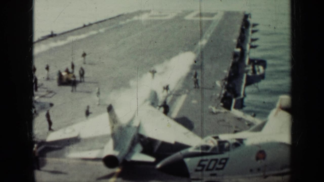 Military jet on an aircraft carrier deck with white exhaust and crew nearby.