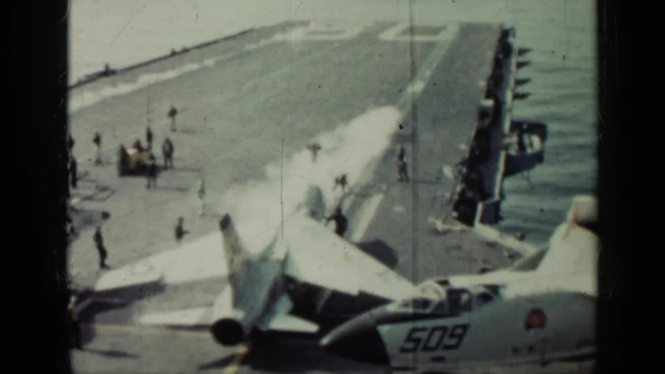 1962 Cuba metadata frame showing a military jet preparing on a carrier deck as crew stand nearby and white exhaust rises behind it.