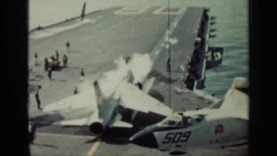 Military aircraft activity on a carrier deck at sea, with crew figures, white exhaust, and aircraft number 509 visible in the foreground.