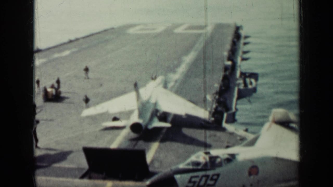 Jet on an aircraft carrier deck with ocean beside the ship and another aircraft marked 509 in the foreground.