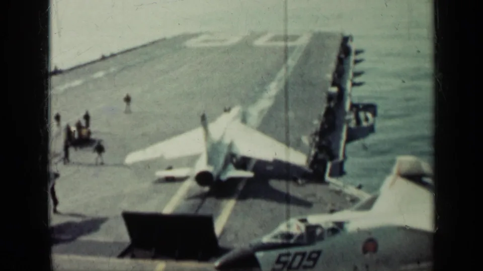 A 1960s military jet appears positioned for carrier deck operations, with crew nearby and another aircraft nose marked 509 in the foreground.