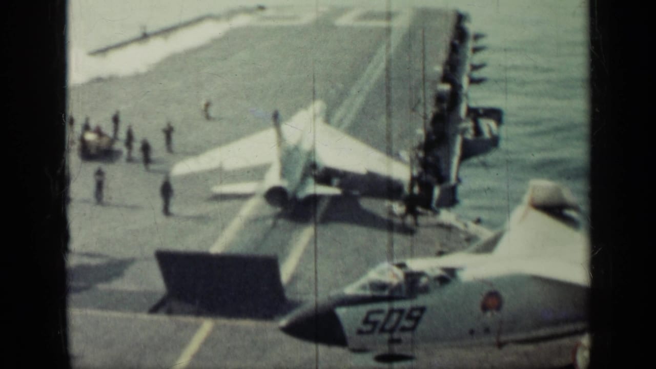 1962-supported carrier deck view near Cuba showing jet aircraft, crew activity, ocean, and visible film frame edges.