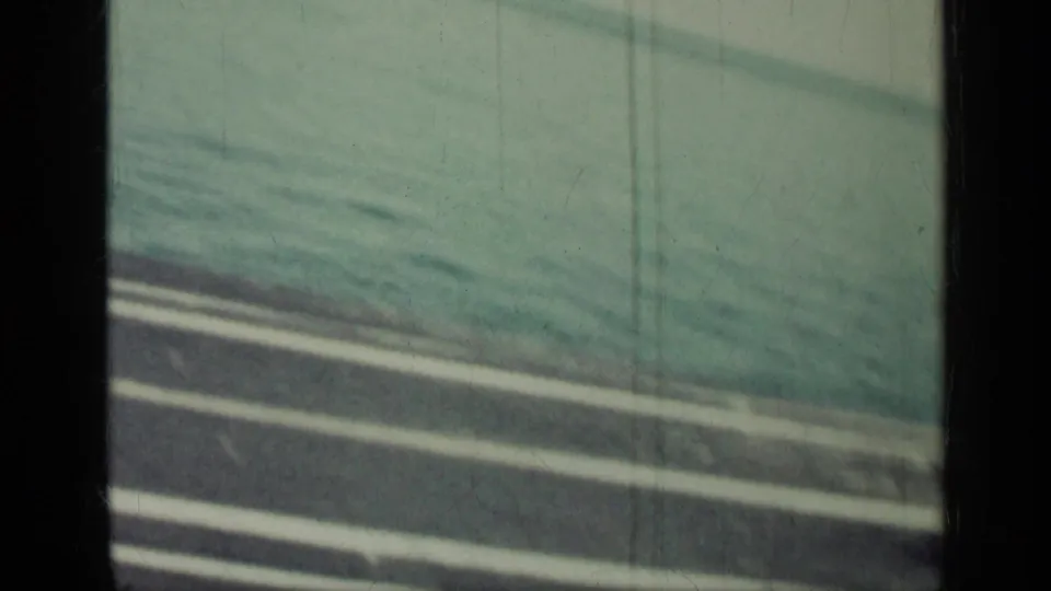 Final frame holds on carrier deck lines and open ocean, with the aircraft largely out of view in scratched 8mm footage.