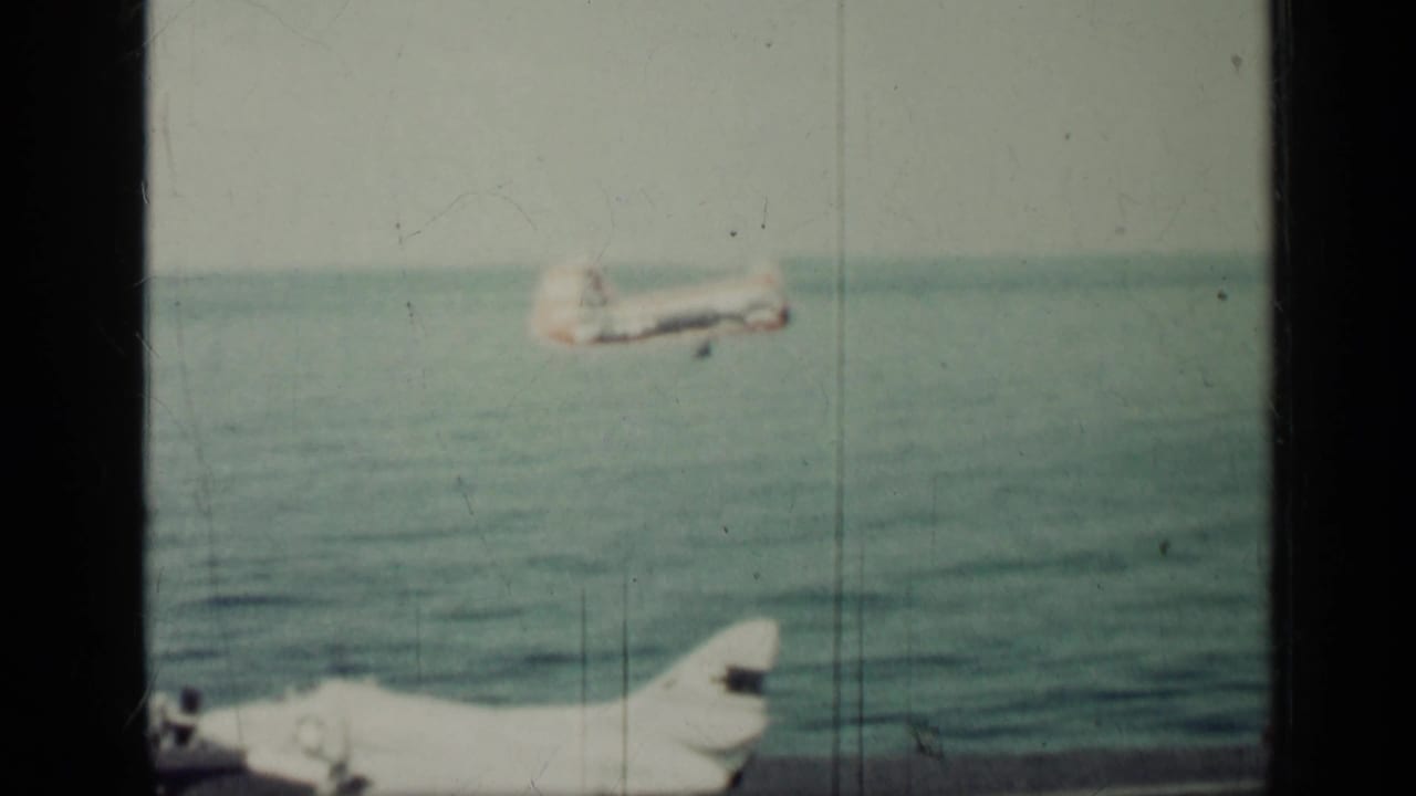 1962 Cuba 8mm frame showing a military aircraft over the sea, with a second aircraft partly visible near the lower edge.