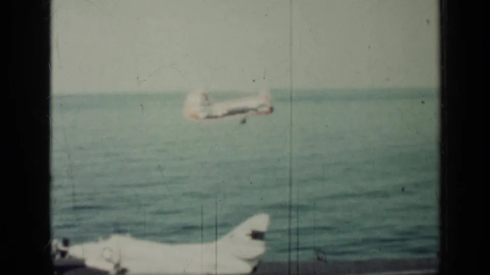 1962 Cuba 8mm frame showing a military aircraft over the sea, with a second aircraft partly visible near the lower edge.
