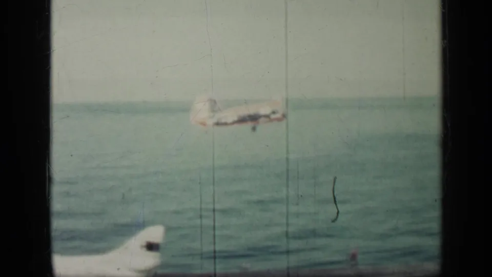 1962 Cuba 8mm frame with a military aircraft in flight over turquoise water and film-frame borders visible.