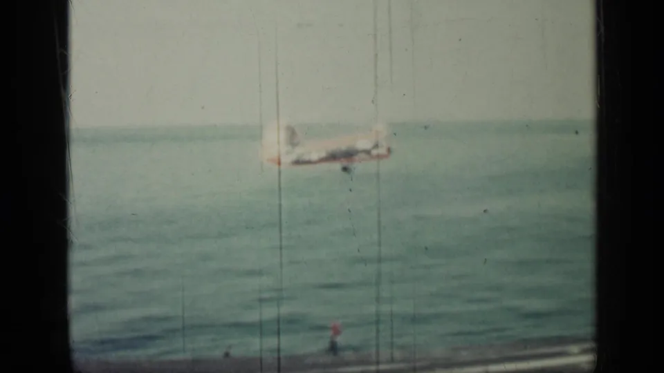 1962 Cuba 8mm frame showing the aircraft farther over open water, with a small lower-edge figure or deck detail visible.