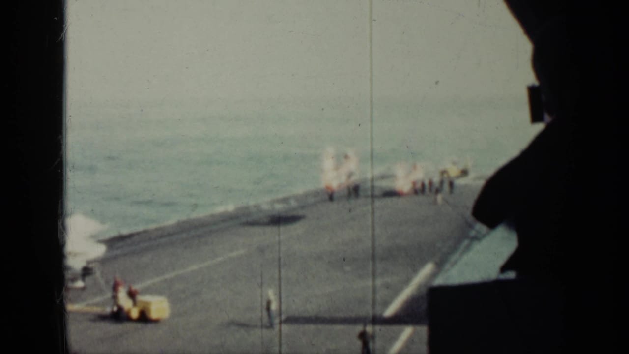 Helicopter and crew on a large ship deck at sea, viewed from behind a dark foreground edge.