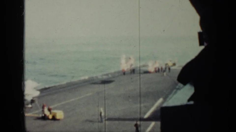 1962 Cuba-labeled 8mm frame showing a helicopter on a warship deck with crew, ocean horizon, and a yellow utility vehicle nearby.