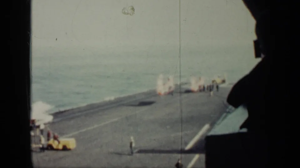 1962 Cuba-labeled frame of a naval deck scene, with crew near a helicopter landing area and a dark ship structure in the foreground.
