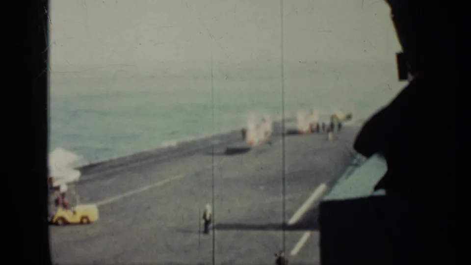 1962 Cuba-labeled 8mm still showing a large warship deck at sea, with a yellow vehicle and crew near the helicopter area.