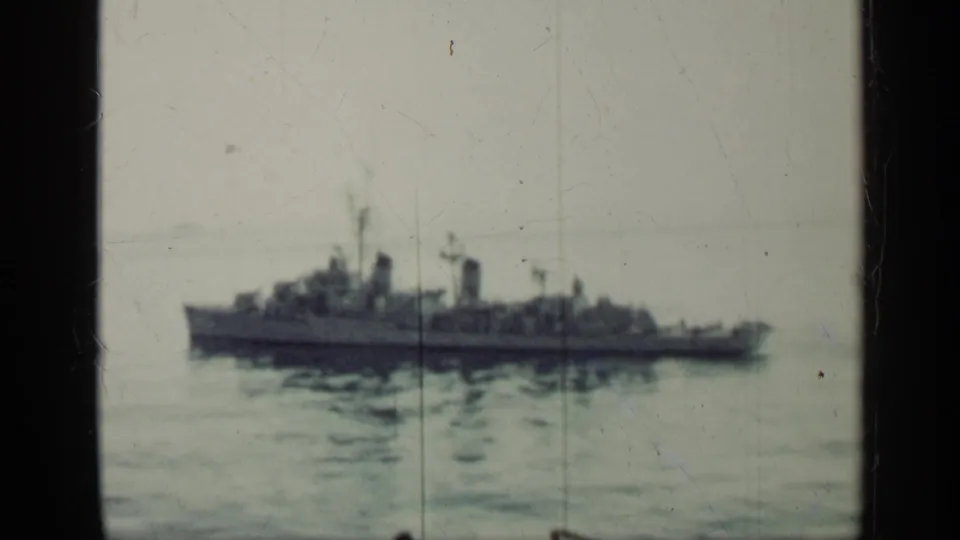 A distant military ship is seen at sea in Cuba-linked 1962 8mm footage, framed by dark telescope-like edges.