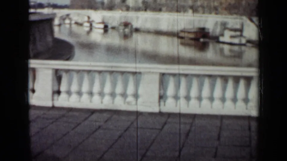 1962 Cuba home-movie frame showing a paved waterfront promenade with a white railing and small houseboats moored beyond.