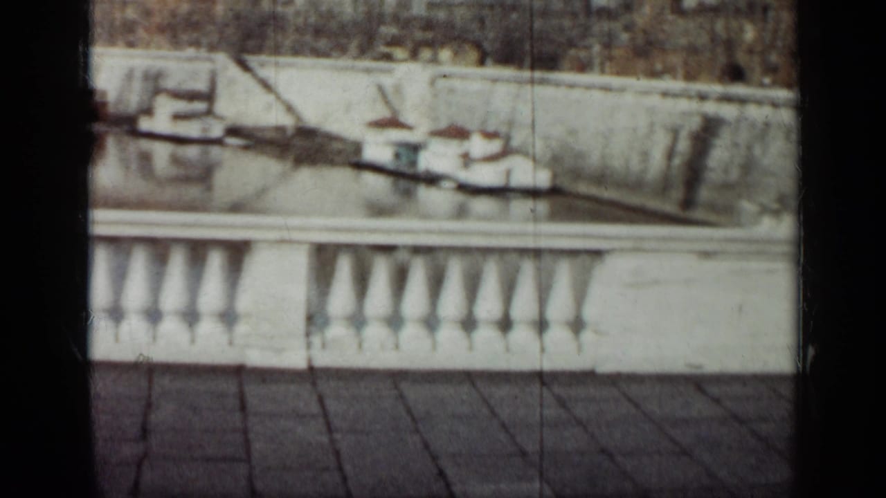 1962 Cuba 8mm frame showing a white waterfront balustrade, tiled foreground, moored boats, and distant buildings across the water.