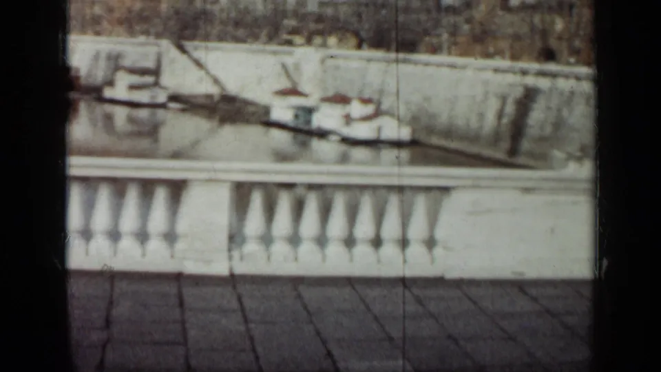 1962 Cuba 8mm frame showing a white waterfront balustrade, tiled foreground, moored boats, and distant buildings across the water.