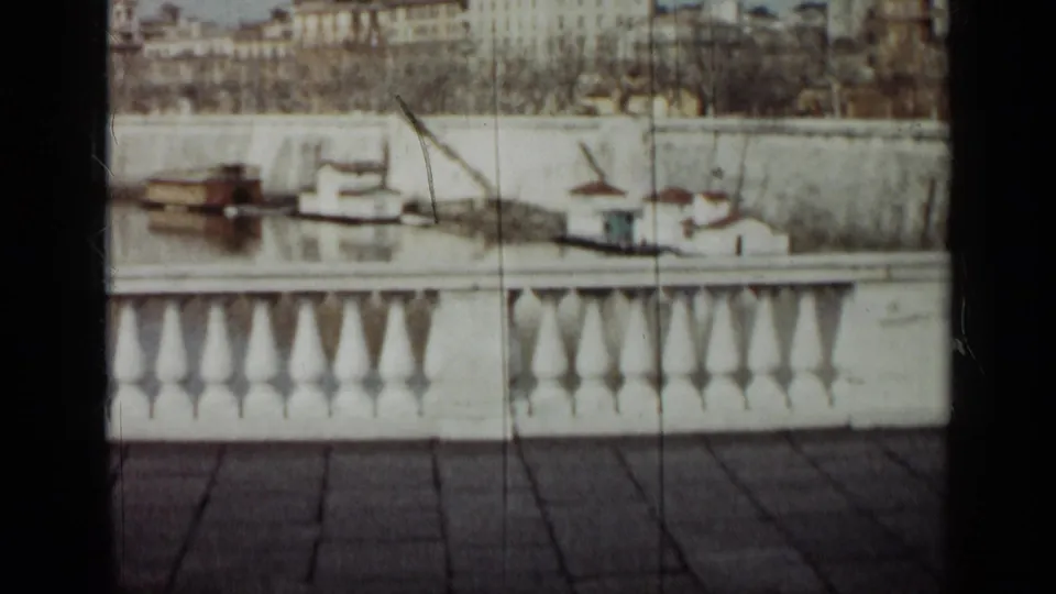 1962 Cuba frame with a white bridge or terrace rail, small boats along the water, and a distant urban riverbank.