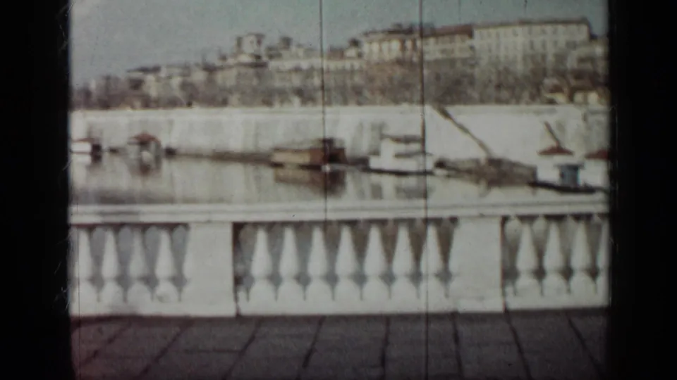 1962 Cuba home-movie frame looking over a white balustrade toward moored boats and a tree-lined urban waterfront.