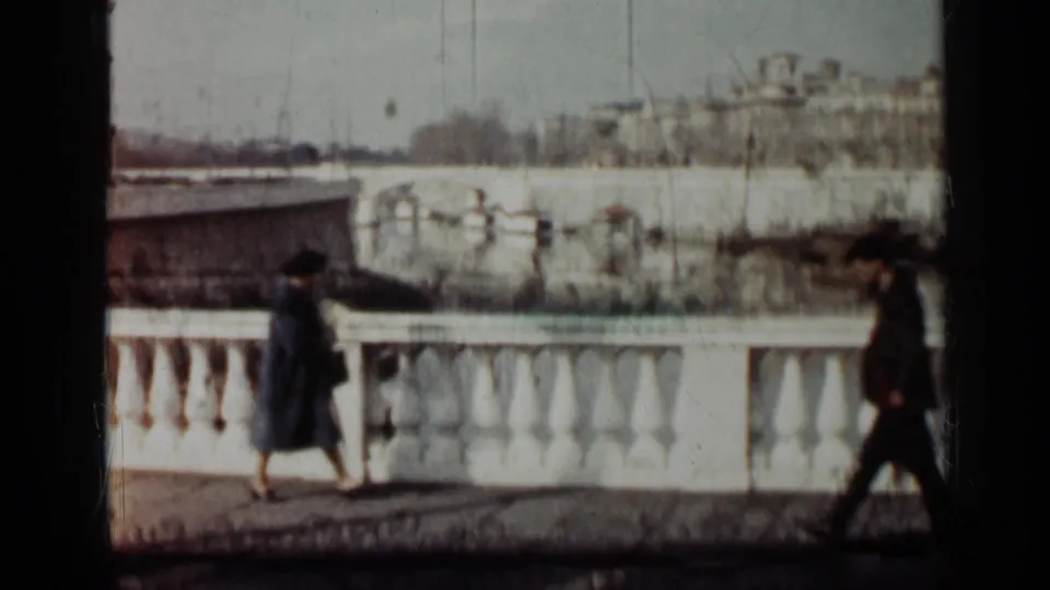 1962 Cuba home-movie frame showing pedestrians near a white bridge or waterfront balustrade with distant buildings beyond.