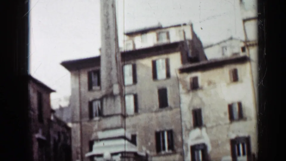 1962 Cuba 8mm frame showing a tall concrete monument rising near shuttered urban buildings in soft focus.