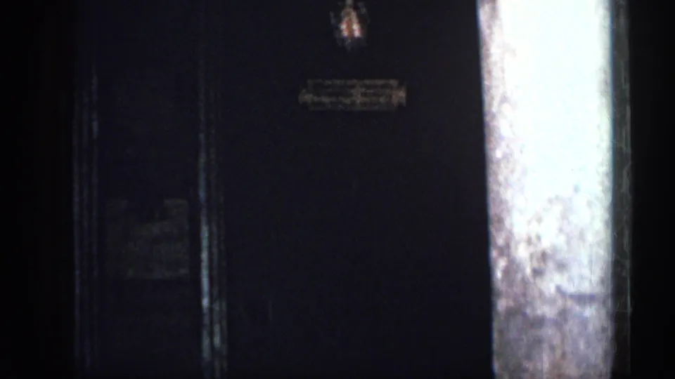 1962 Cuba 8mm frame showing a shadowed entrance or wall next to a large column, with signage too soft to read.