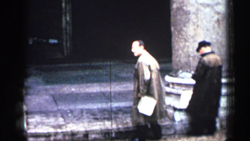 1962 Cuba 8mm frame showing two men near a column and steps, one holding a light-colored paper or bag.