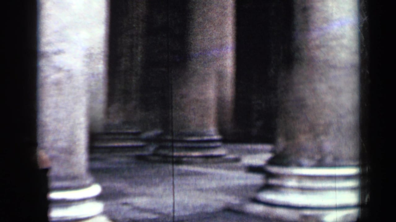 Soft-focus stone columns and bases inside a dark classical building.
