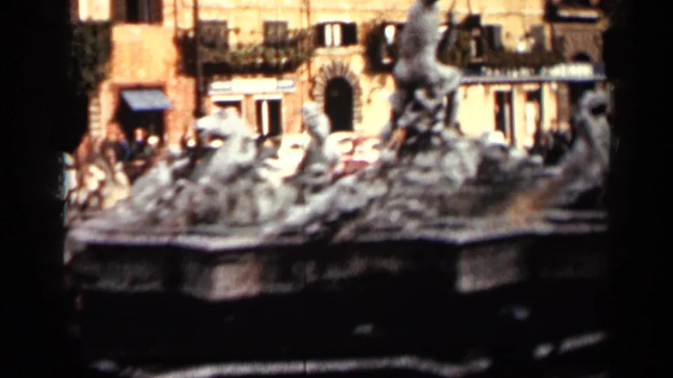 Stone fountain sculptures stand before a Cuban public square scene with mid-century cars, pedestrians, balconies, and arched entrances.