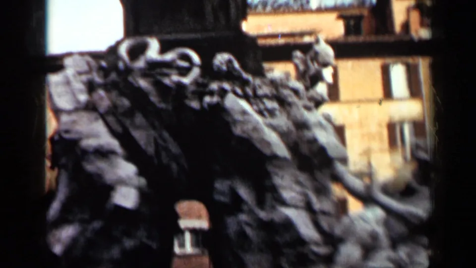 1962 Cuba frame with the camera close to the fountain's carved stone forms, backed by warm city facades and windows.