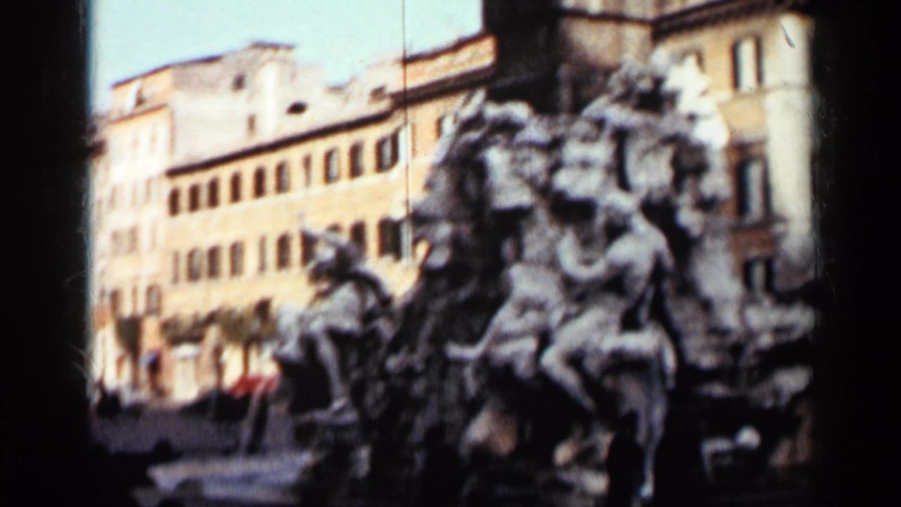 Soft 8mm view of an elaborate fountain sculpture, likely in Rome per clip notes, with historic facades behind it.