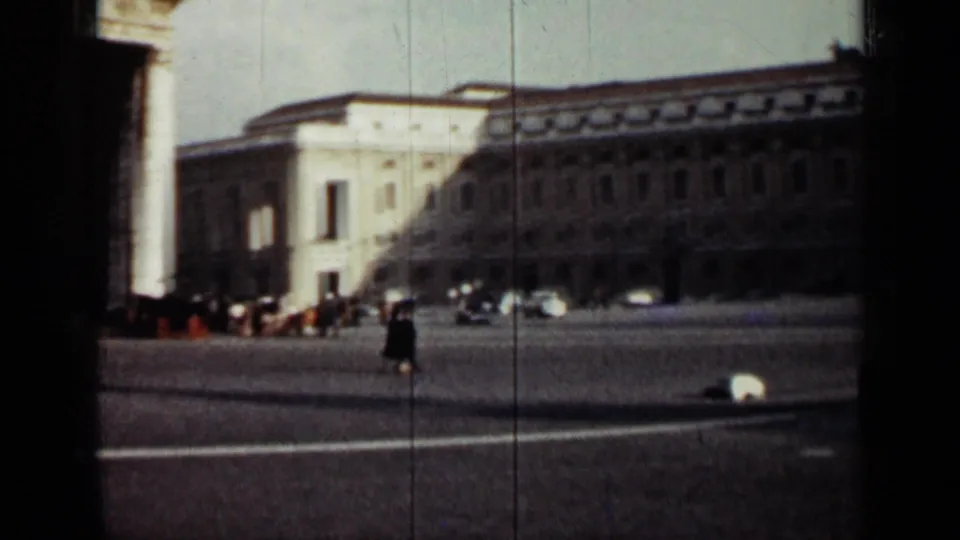 1962 Cuba travel footage frame showing a broad public square, landmark-scale buildings, cars, and a distant pedestrian.