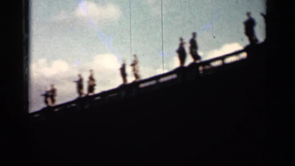1962 Cuba 8mm frame with silhouetted visitors spaced along a sloping balustrade, with sky and clouds behind them.