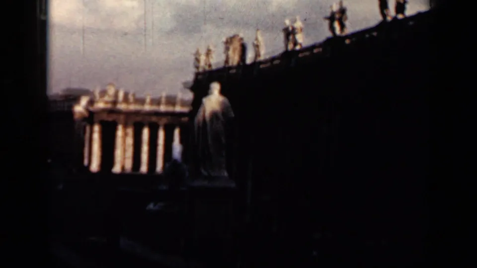 1962 Cuba 8mm frame showing a statue, colonnaded building details, and silhouetted pedestrians above a dark foreground.