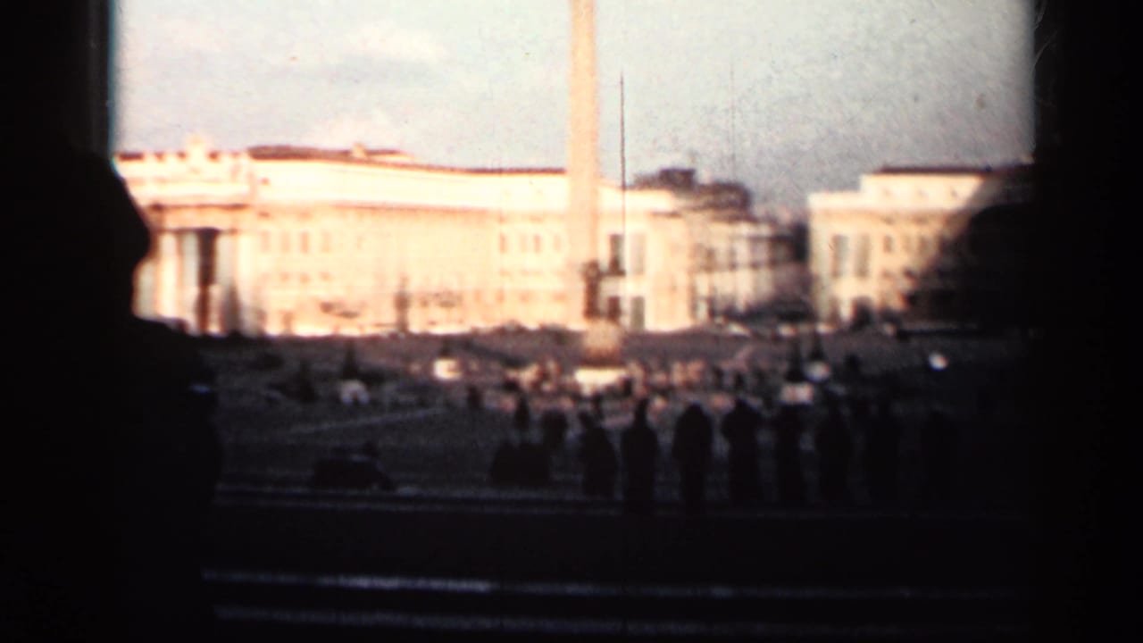 Wide view of a sunlit palace facade and plaza seen through dark foreground framing.