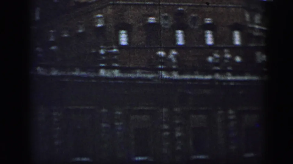 1962 Cuba frame of a shadowed building exterior, with upper windows, decorative roofline figures, and a mostly dark street level.