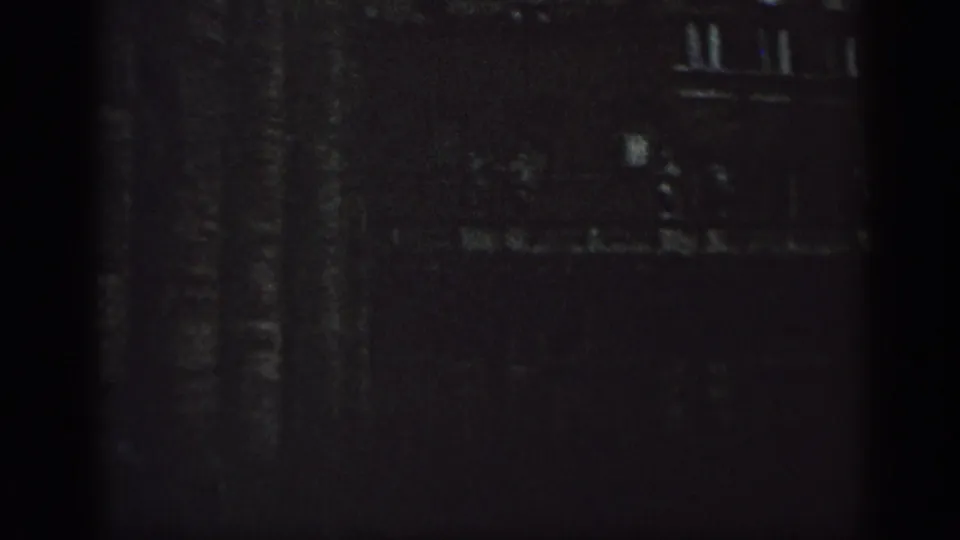 1962 Cuba home-movie frame showing a barely lit section of an older building with faint windows and shadowed masonry texture.
