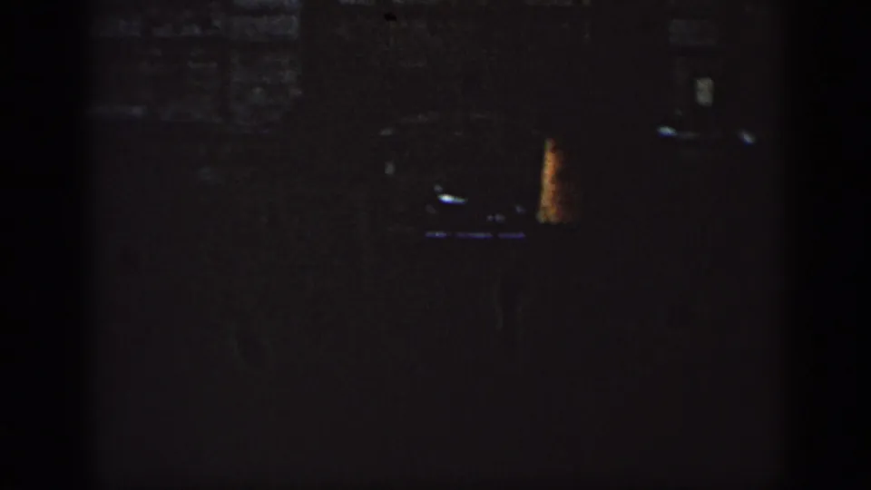 Opening 8mm frame is mostly dark, with a small bright architectural detail and strong gate shadows at the edges.