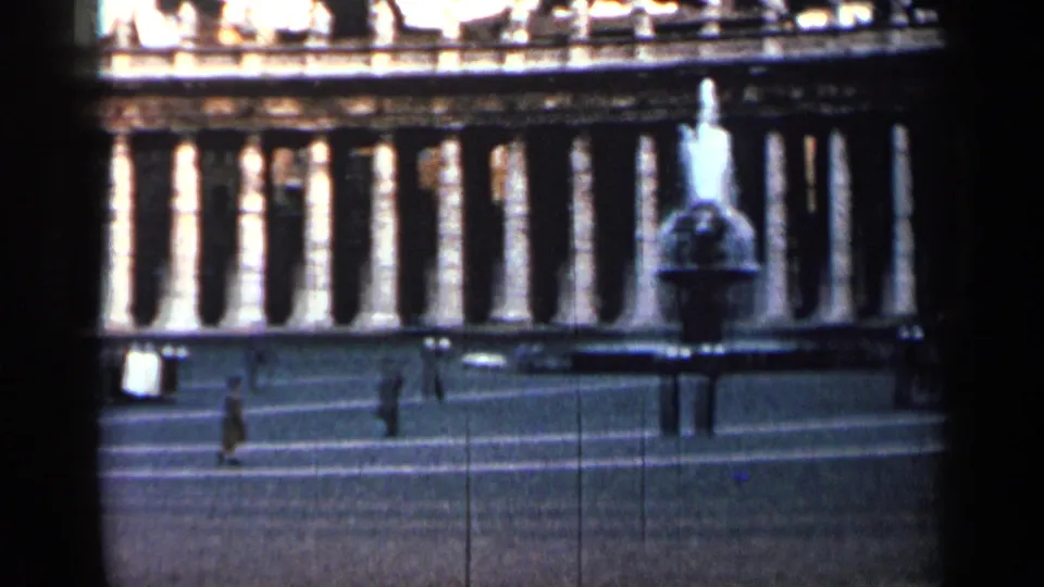 1962 Cuba 8mm frame with a fountain or monument in front of a long colonnade and pedestrians crossing the open square.