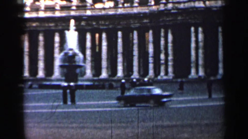 1962 Cuba 8mm frame showing a fountain or monument, colonnaded backdrop, pedestrians, and a mid-century car moving through the square.