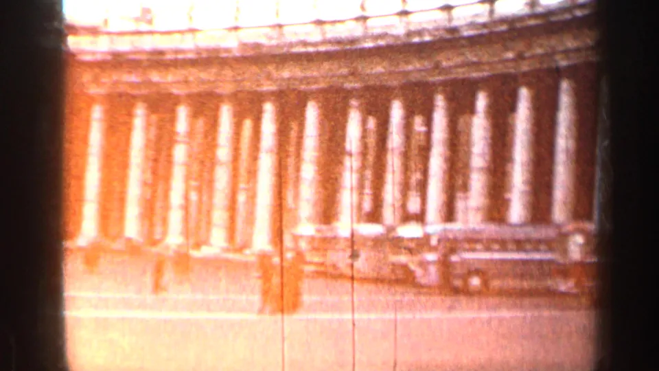 Warm 8mm frame from Cuba in 1962 showing a sunlit colonnade and a bus or large vehicle moving through the plaza view.