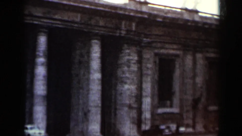1962 8mm travel footage showing a stone architectural facade with columns, windows, and dark gate-like shadows at the frame edges.