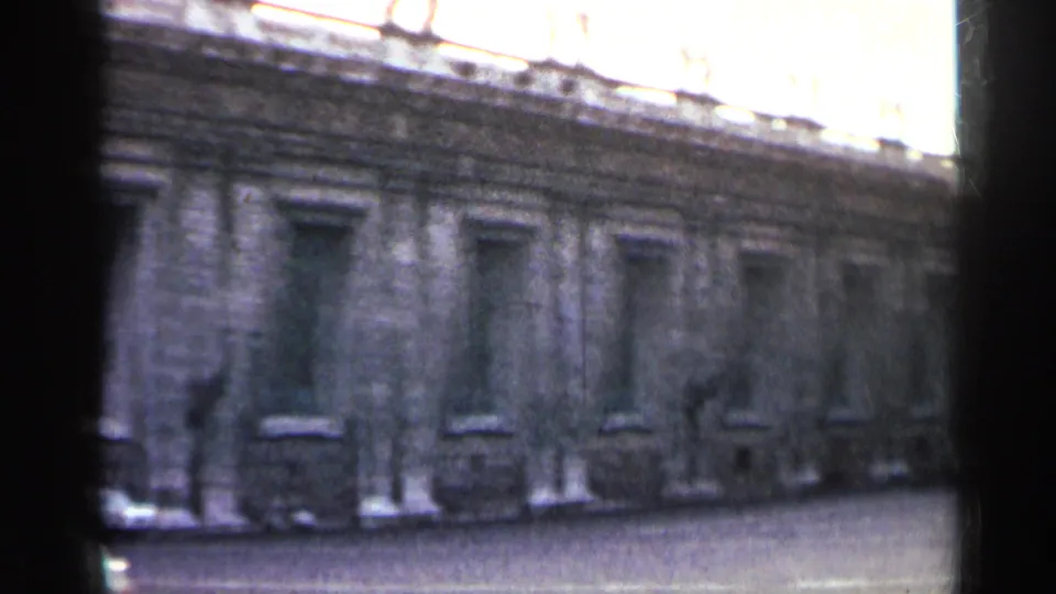 Cataloged 1962 footage of a long monumental stone facade with repeated windows, seen in soft focus through dark film-frame shadows.
