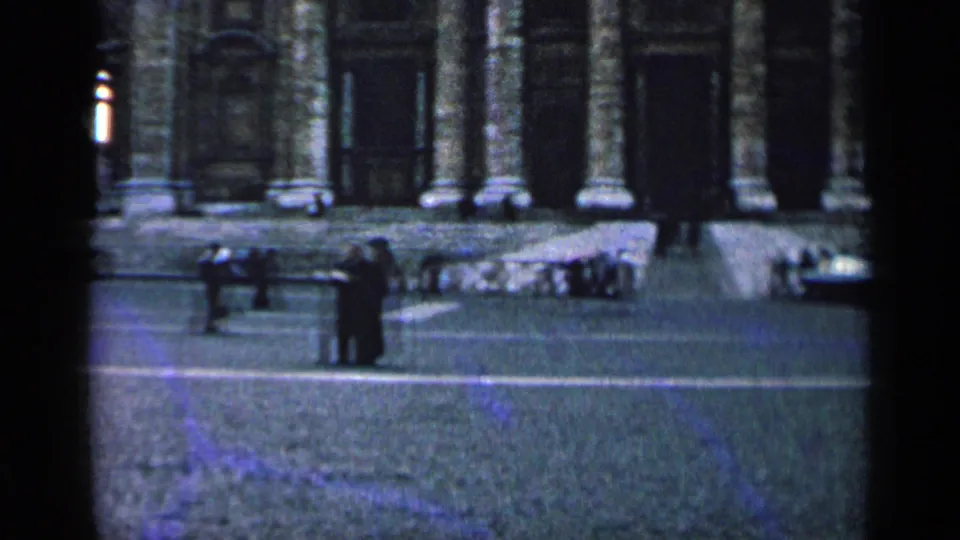 1962 8mm view of a monumental church-like entrance with columns and steps, with small groups of people standing in the plaza.