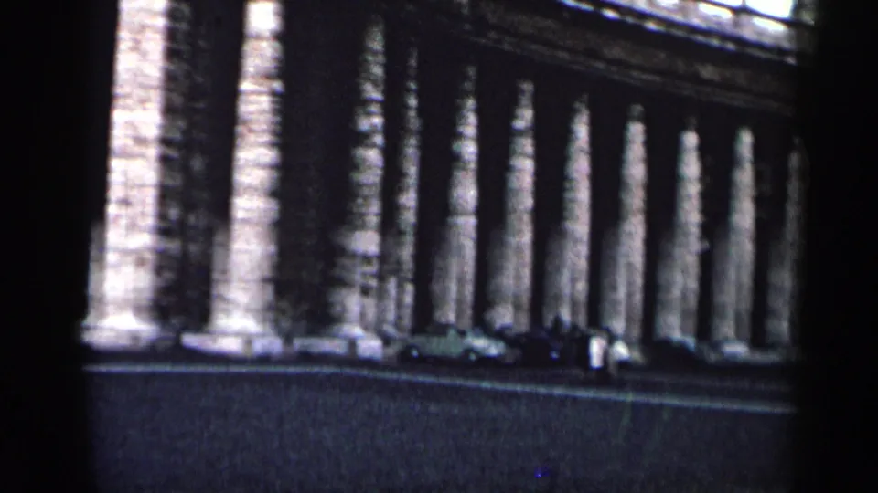 1962 Cuba street view of a long stone colonnade with mid-century cars parked in front.