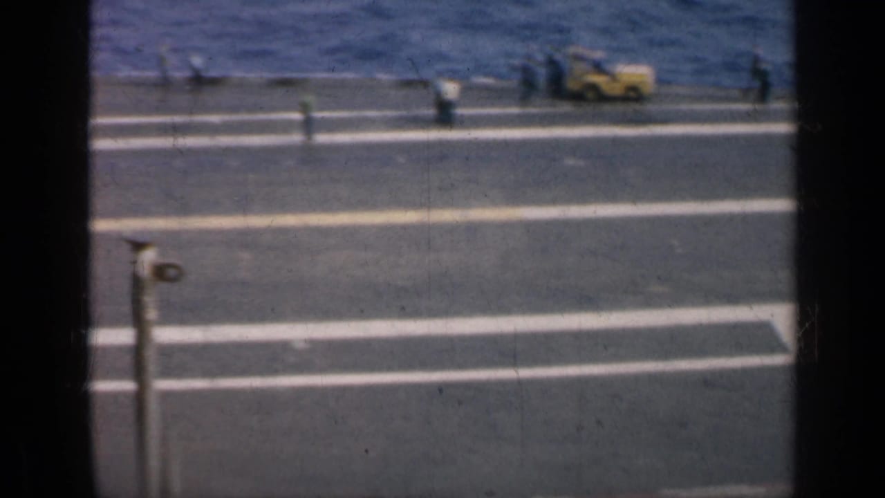 1962 Cuba 8mm footage looking down from an aircraft carrier, with deck markings, distant crew, and the sea beyond the ship edge.