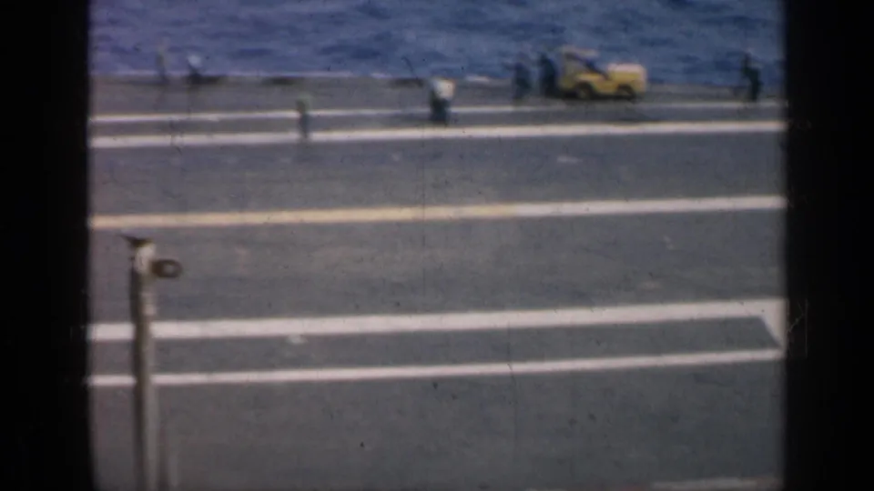 1962 Cuba 8mm footage looking down from an aircraft carrier, with deck markings, distant crew, and the sea beyond the ship edge.