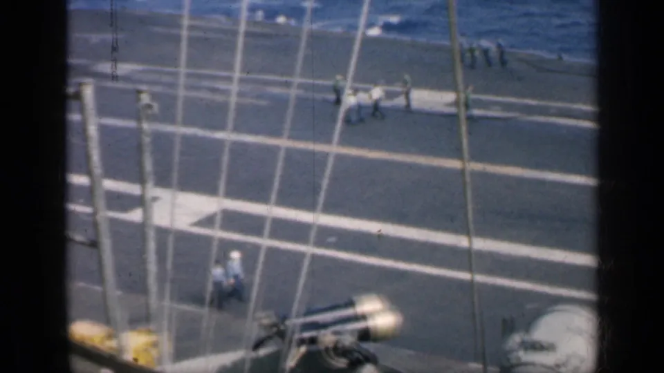 1962 Cuba carrier deck scene with crew on marked pavement, mast lines or cables in front, deck lamps, and a yellow service vehicle near the lower edge.