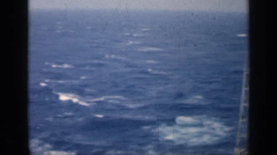 1962 Cuba 8mm frame of rough blue water with white foam patches, viewed through dark ship-window or film-edge framing.
